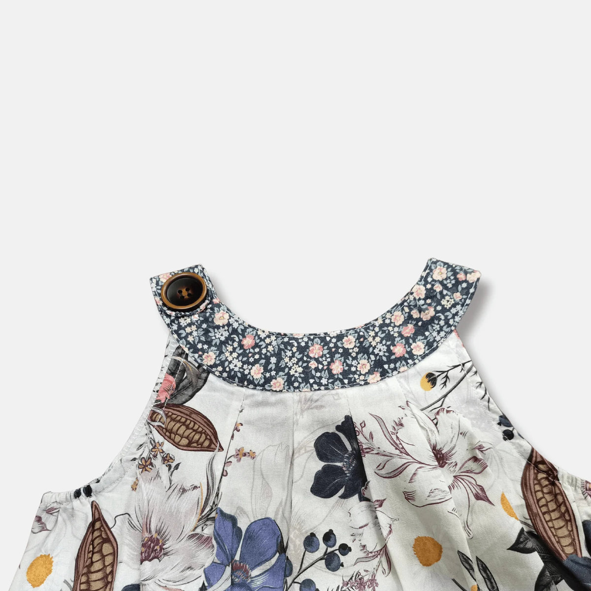 Close-up of a children's floral dress with a white base, navy blue floral collar, and a brown button closure, shown against a light gray background.