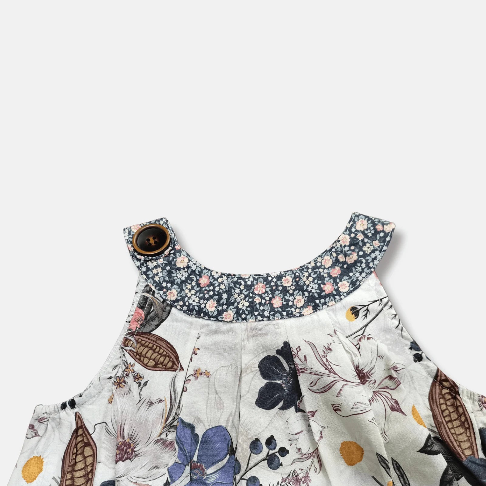 Close-up of a children's floral dress with a white base, navy blue floral collar, and a brown button closure, shown against a light gray background.