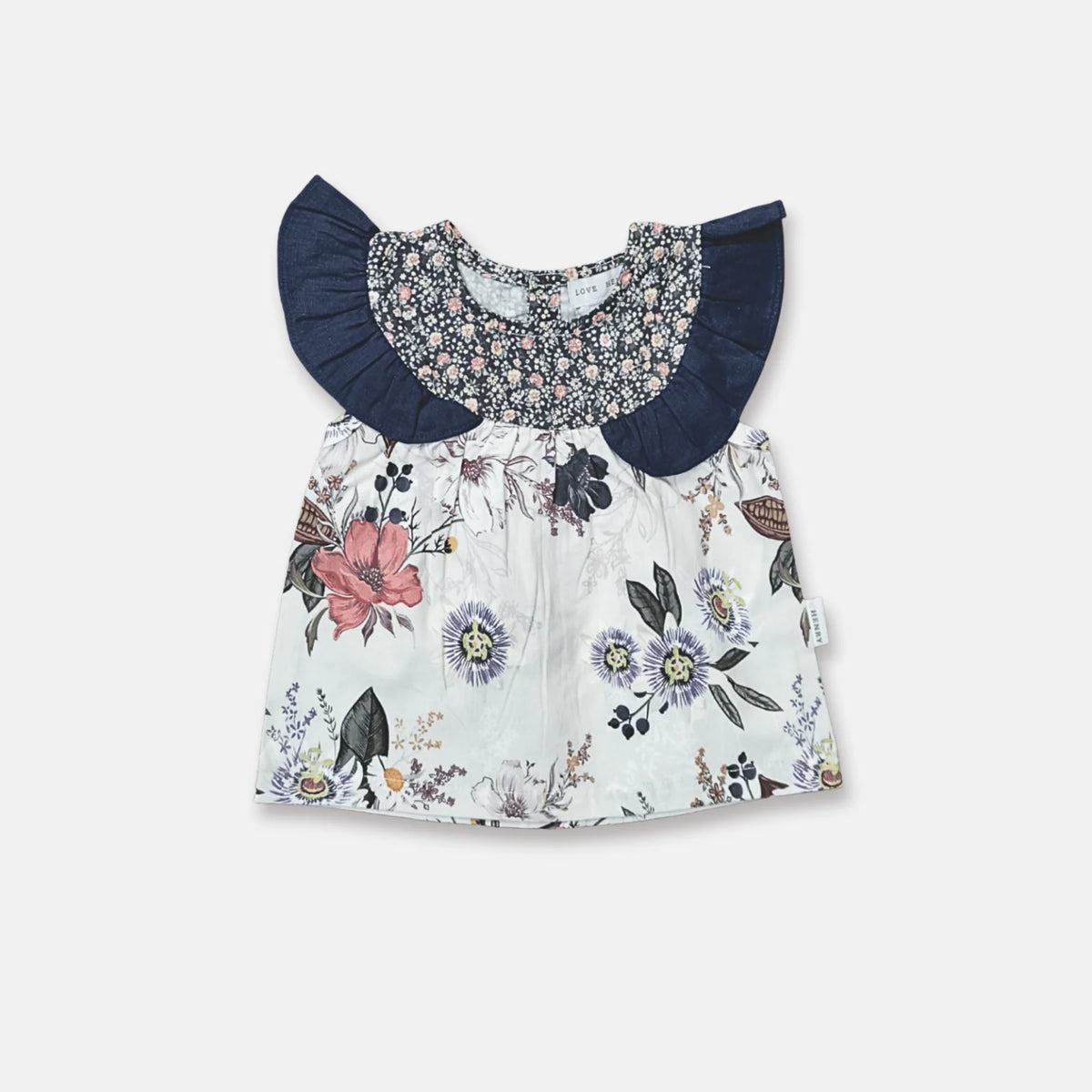 A baby girl's short-sleeve dress with a white floral print body, a navy blue ruffled collar, and a matching navy smocked yoke with a small floral pattern.