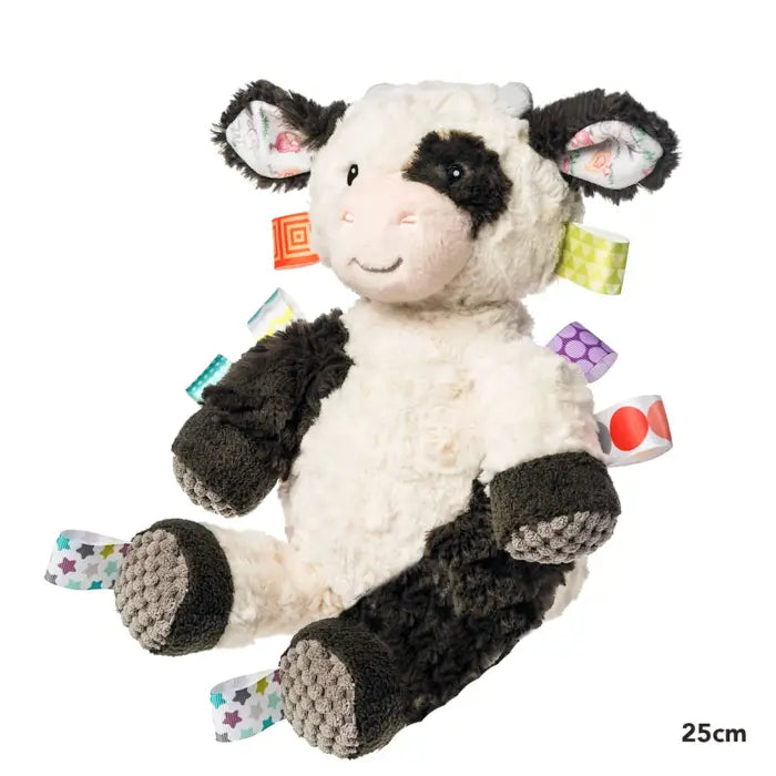 A plush cow baby toy with a white and black body, patterned ears, and colorful textured latches on the sides, photographed on a solid white background.