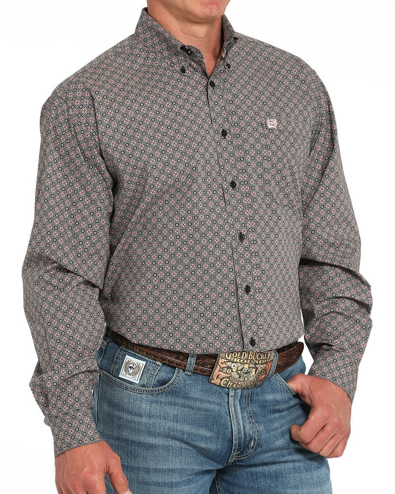 A man wearing a long-sleeve button-down shirt with a small geometric pattern in gray, beige, and red, paired with blue jeans and a western belt.