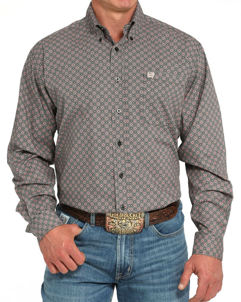 A man wearing a long-sleeve button-down shirt with a small geometric pattern in gray, beige, and red, paired with blue jeans and a western belt.