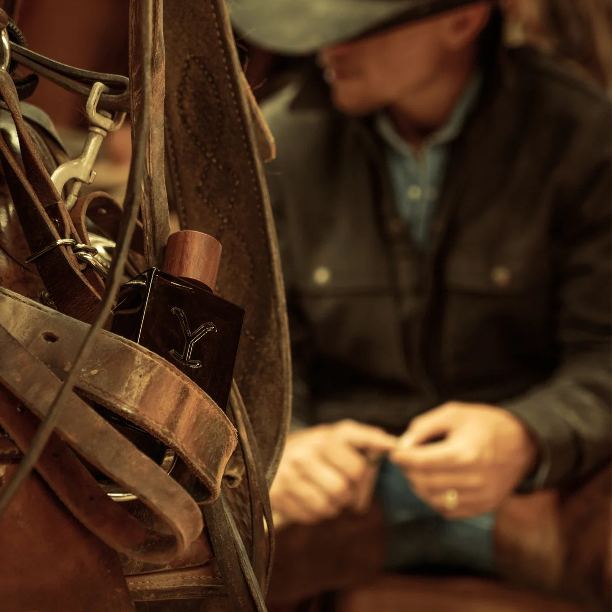 Close-up of a leather saddle with a person adjusting it in the background