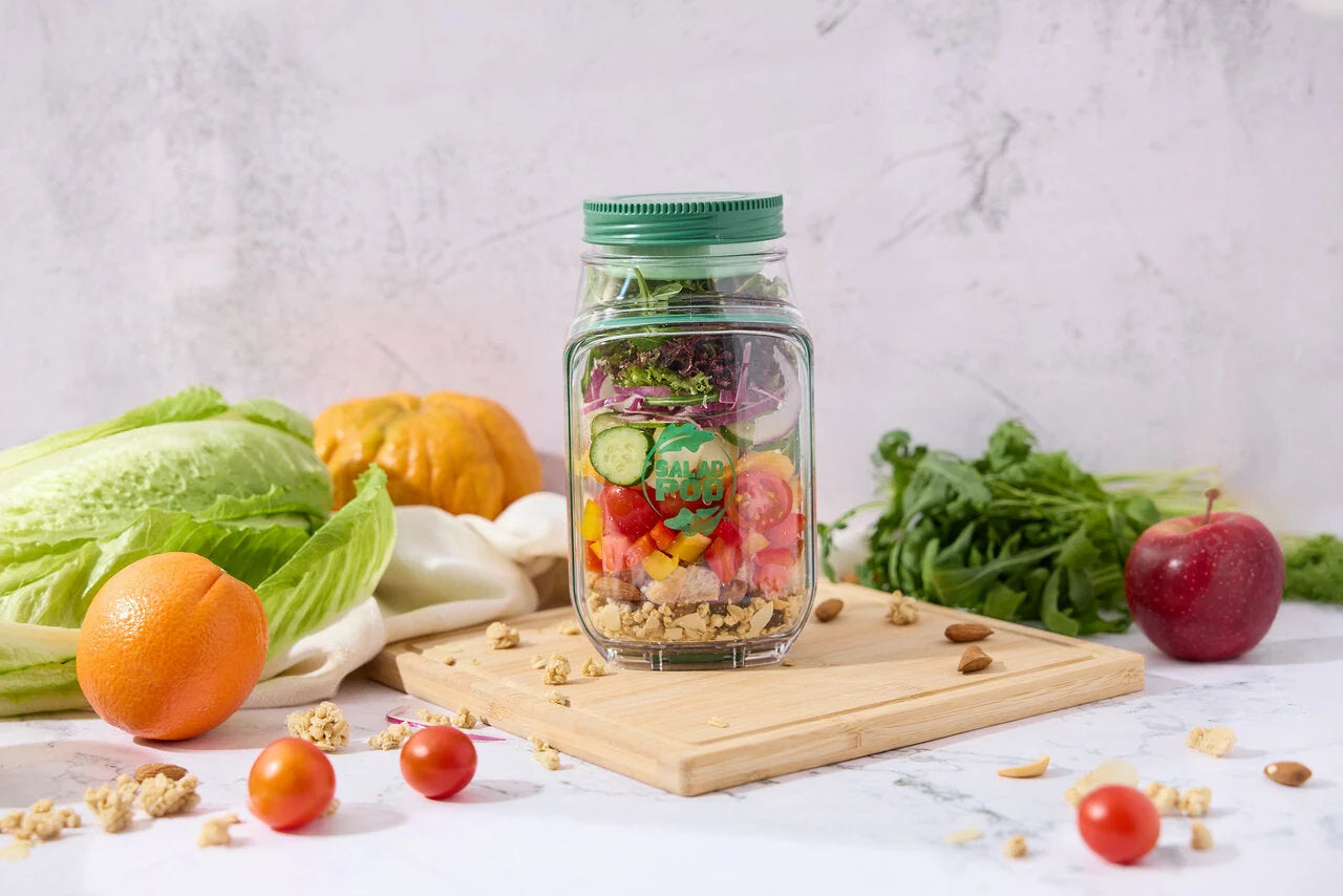 Glass jar with salad ingredients on a wooden board surrounded by fresh produce on a light background