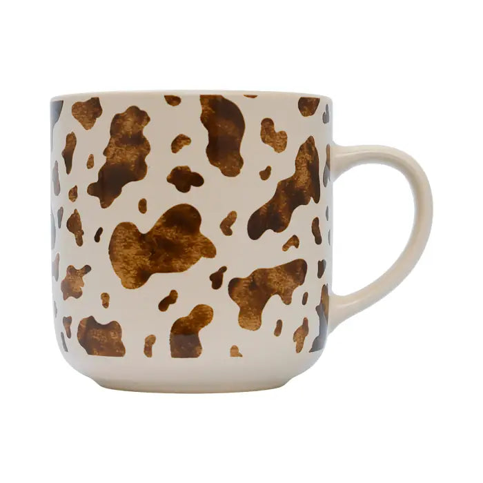 A ceramic coffee mug with a brown and gold cow print pattern on a cream background, featuring a sturdy handle on the right side.