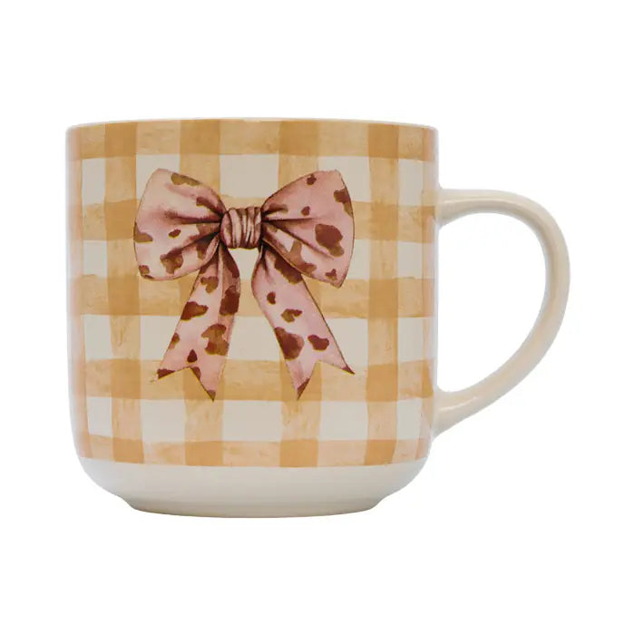 A ceramic mug with a warm yellow and cream gingham pattern, decorated with a pink and brown spotted bow illustration on the front, set against a plain white background.