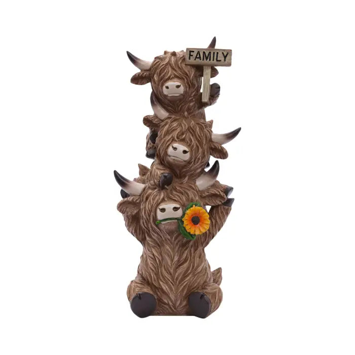 A stacked figurine of four Highland cows in brown and beige tones, with the top cow holding a wooden sign that says FAMILY and the bottom cow holding a yellow sunflower, on a plain white background.