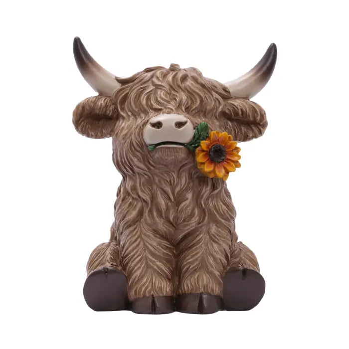 A sculpted Highland cow figurine with long brown hair, curved horns, and a yellow sunflower in its mouth, set against a plain white background.