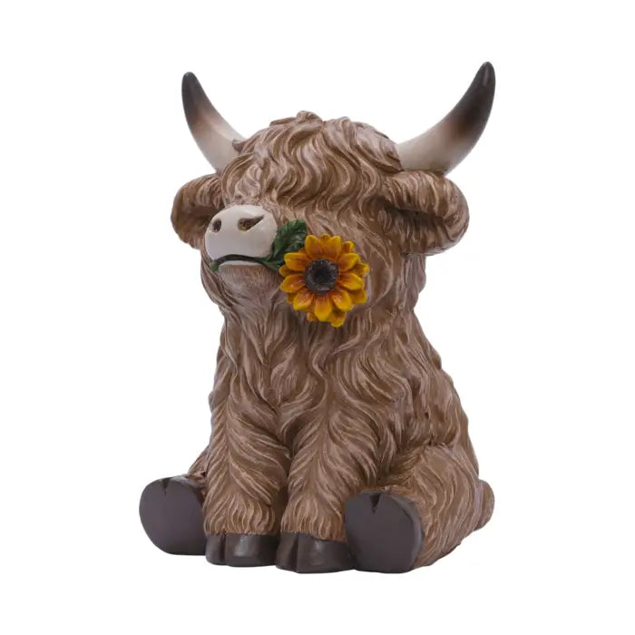 A Highland cow figurine with shaggy brown fur, curved horns, and a yellow sunflower tucked into its mouth, set against a plain white background.