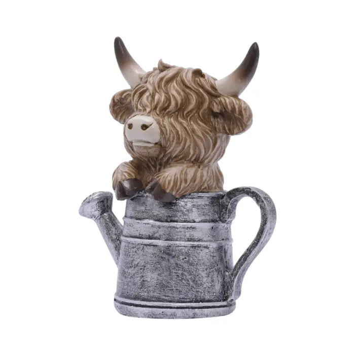 A decorative figurine of a shaggy brown Highland cow with horns sitting inside a weathered gray watering can, shown on a plain white background.