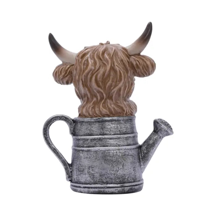 A decorative figurine of a Highland cow with long shaggy brown hair and curved horns, positioned inside a distressed silver metal watering can, shown against a plain white background.