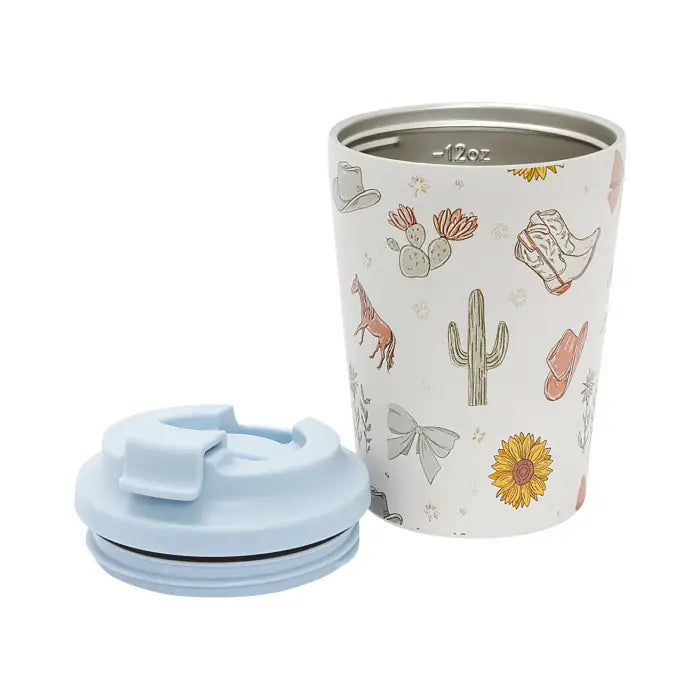 A stainless steel travel tumbler with a white background and a western-themed print featuring cacti, cowboy boots, hats, and a sunflower, shown next to its light blue lid on a white background.