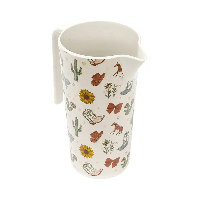 An off-white ceramic pitcher with a western-themed print featuring cowboy boots, cacti, sunflowers, horseshoes, and horses.
