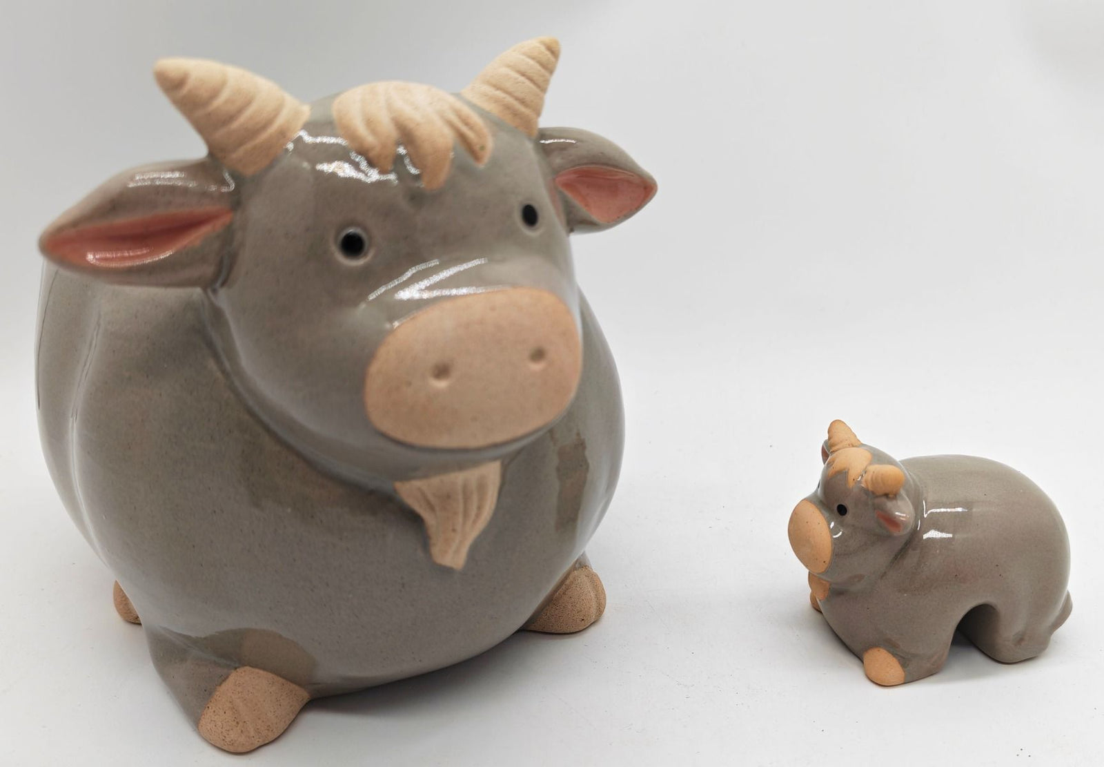 A glossy ceramic cow figurine with a smaller matching cow beside it, photographed on a plain white background.
