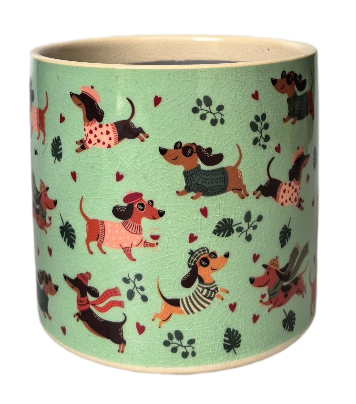 A cylindrical ceramic planter or cup with a light mint green textured exterior, decorated with a playful pattern of dachshunds in various outfits, hearts, and leaves. The interior and rim are cream-colored.
