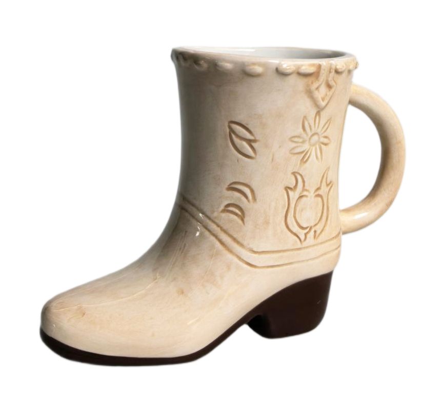 A ceramic mug shaped like a western cowboy boot, featuring a cream-colored body with embossed western-style floral and leaf patterns, a dark brown block heel, and a matching cream handle on a white background.