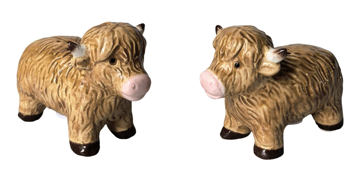 Two ceramic Highland cow figurines shown side by side on a plain white background, one facing left and one facing right. The figurines have textured tan and brown fur, pink snouts and ears, and dark brown hooves.