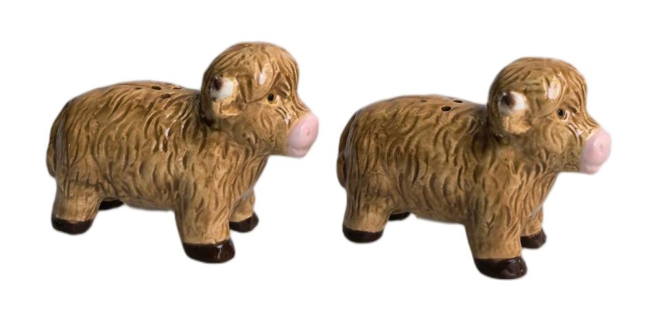 A pair of ceramic salt and pepper shakers shaped like Highland cows, featuring textured brown bodies, pink noses, and dark brown hooves, set against a plain white background.