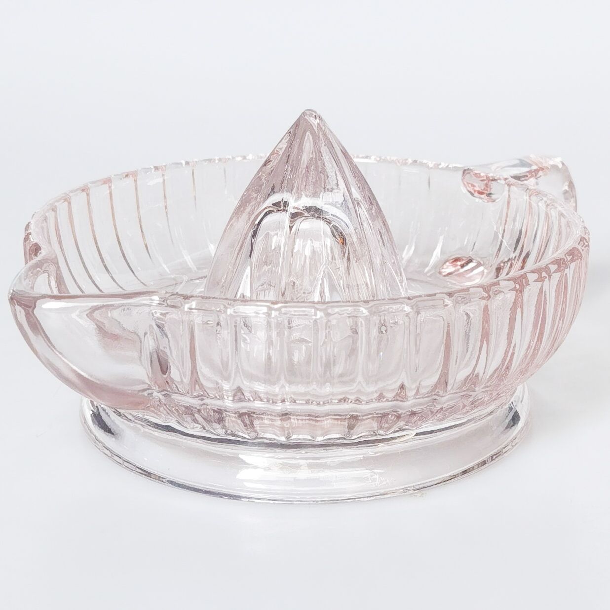 A clear glass citrus juicer with a ribbed bowl, handle, and central reamer cone, shown on a plain light gray background.