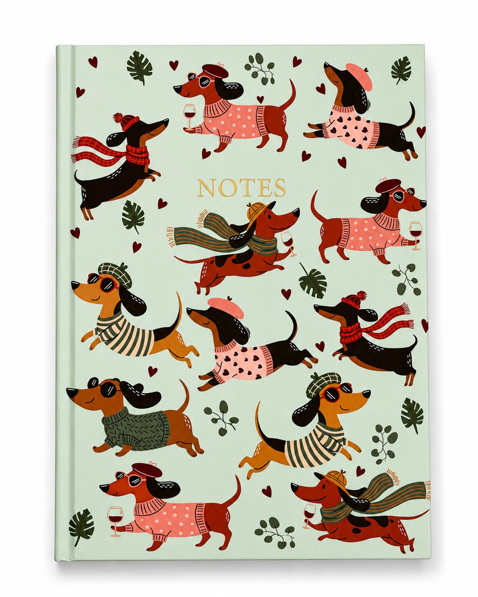 A mint green hardcover notebook with a whimsical illustration of dachshunds wearing winter clothing, scattered red hearts, and the word 'NOTES' printed in gold near the top center.